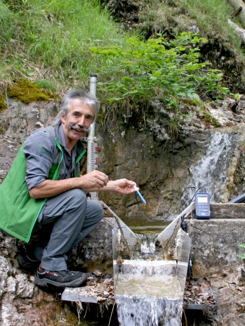 Zaměstnanec národního parku měří teplotu vody v malém horském kanálu ve strmém terénu