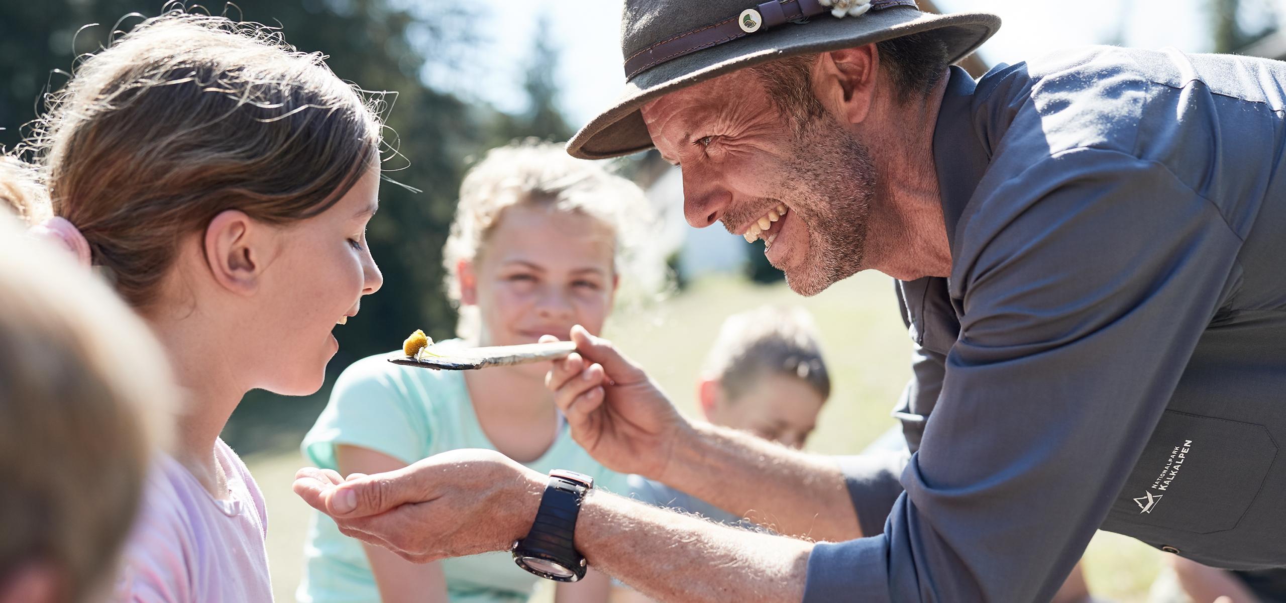 Strážce národního parku podává dívce jídlo na dřevěné lžíci