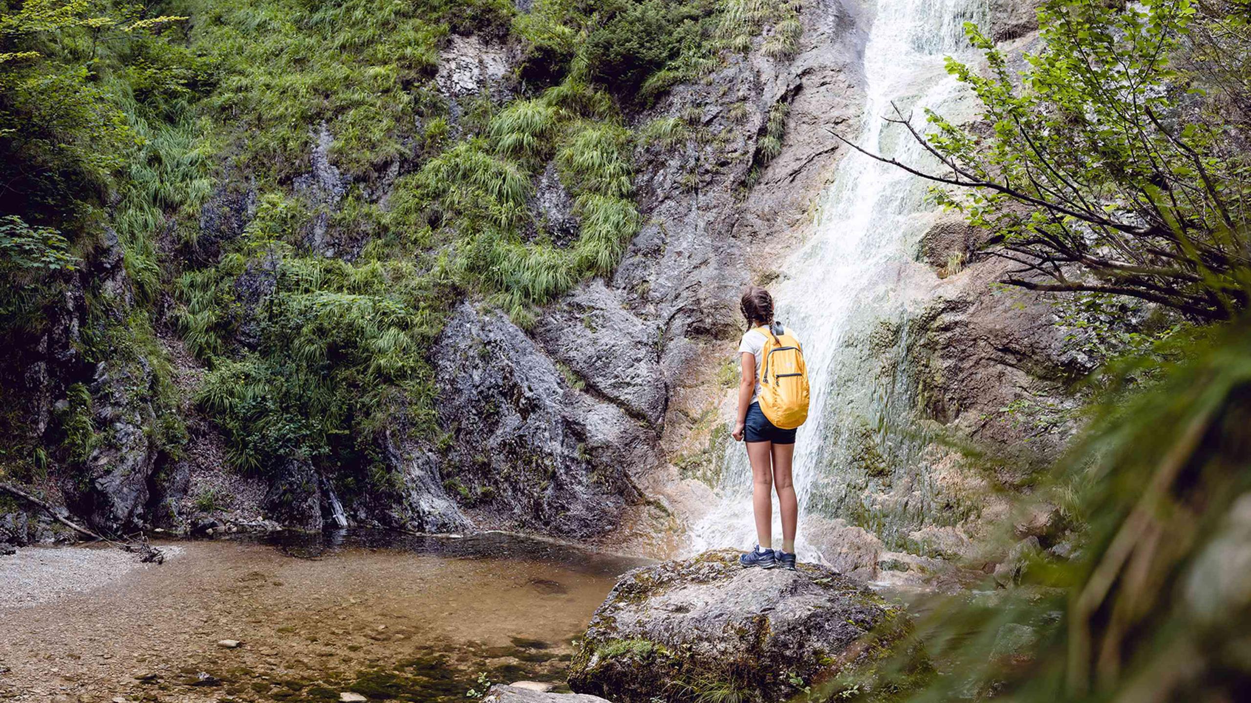 Žena stojí na skále před vodopádem