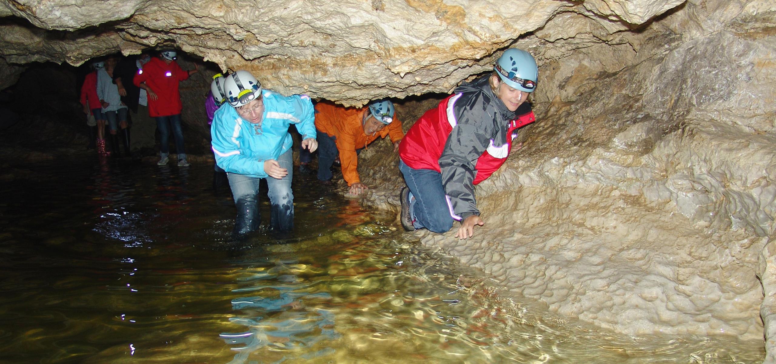 Děti i dospělí se tlačí podél stěny jeskyně.