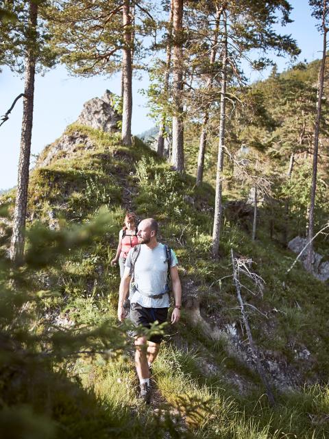 Žena a muž jdou po úzké stezce ve skalnatém lese.